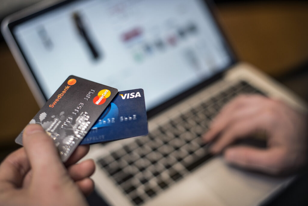 Närbild på två bankkort, ett Swedbank och ett Visa. I bakgrunden knappar någon på en dator.