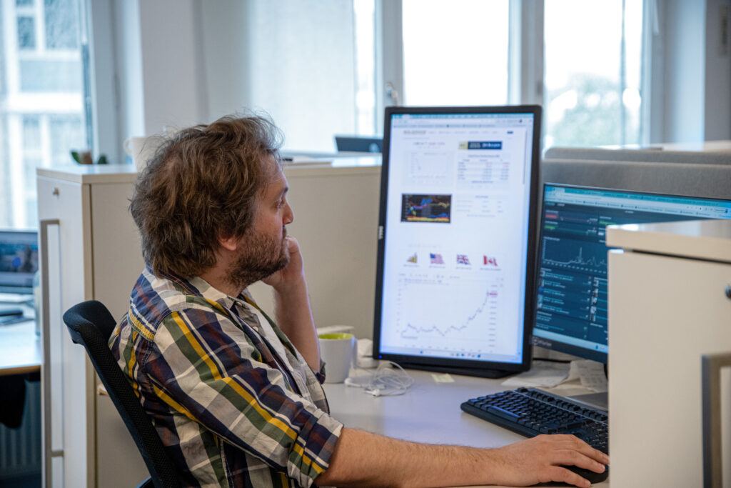 Alexander Piauger sitter vid ett skrivbord i kontorslandskap. Han tittar mot den ena av de två datorskärmarna på skrivbordet.